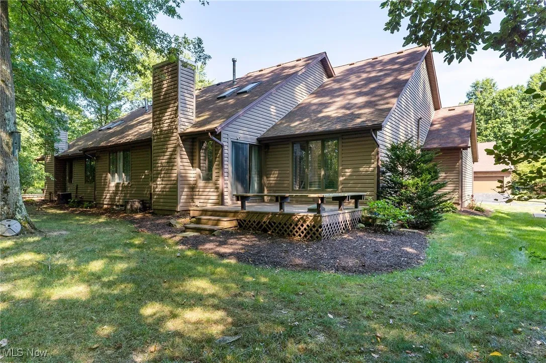 Rear view of property featuring a wooden deck, a chimney, a shingled roof, and a yard