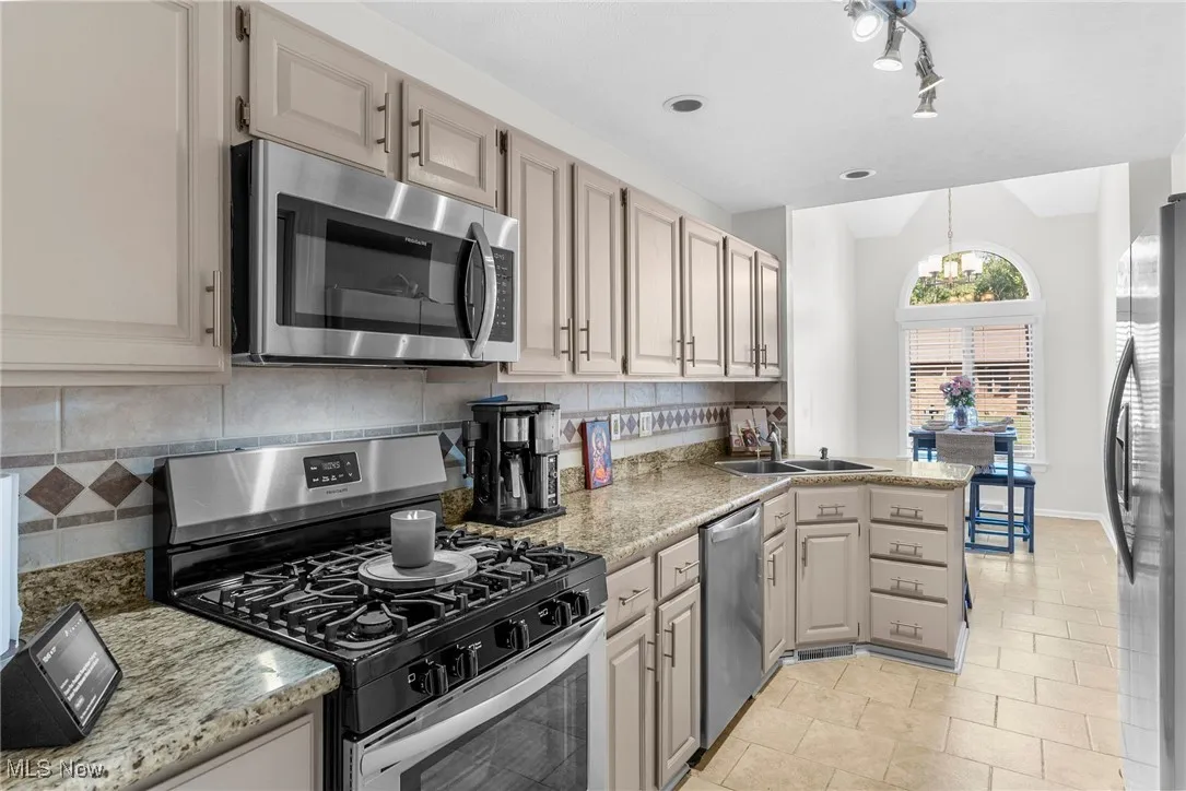 Kitchen featuring stainless steel appliances, backsplash, decorative light fixtures, a peninsula, and light tile patterned flooring
