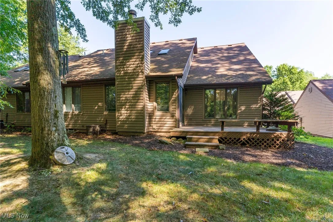 Back of house with a wooden deck, roof with shingles, a chimney, and a lawn