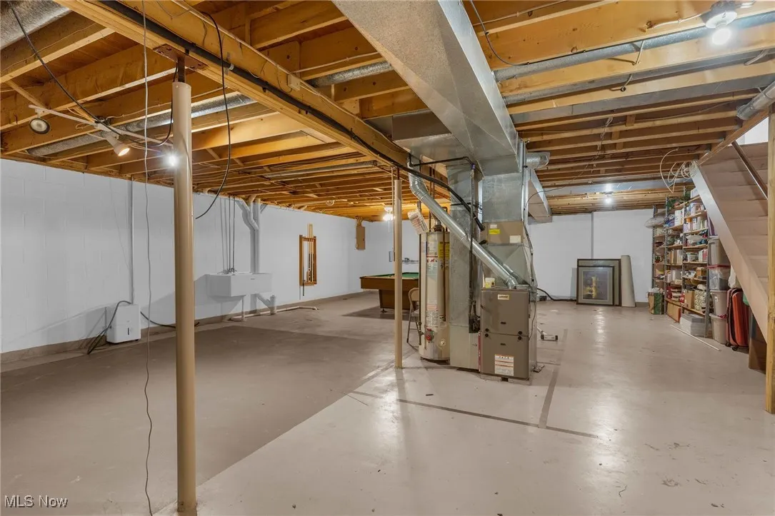 Unfinished below grade area with gas water heater, heating unit, and pool table