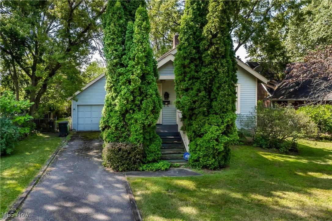 View of property hidden behind natural elements with a front lawn, an outdoor structure, driveway, and a garage