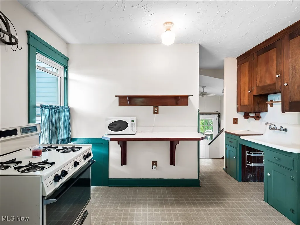 Kitchen with white appliances, open shelves, light countertops, green cabinetry, and a textured ceiling