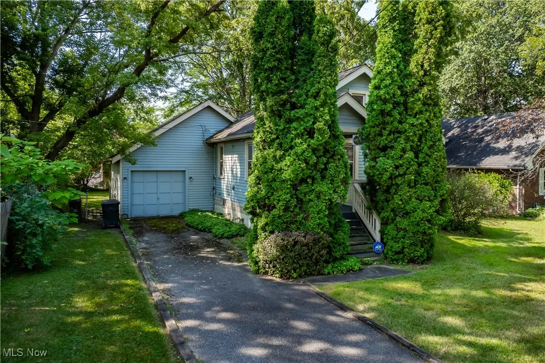 View of property hidden behind natural elements featuring driveway, a front yard, and a garage