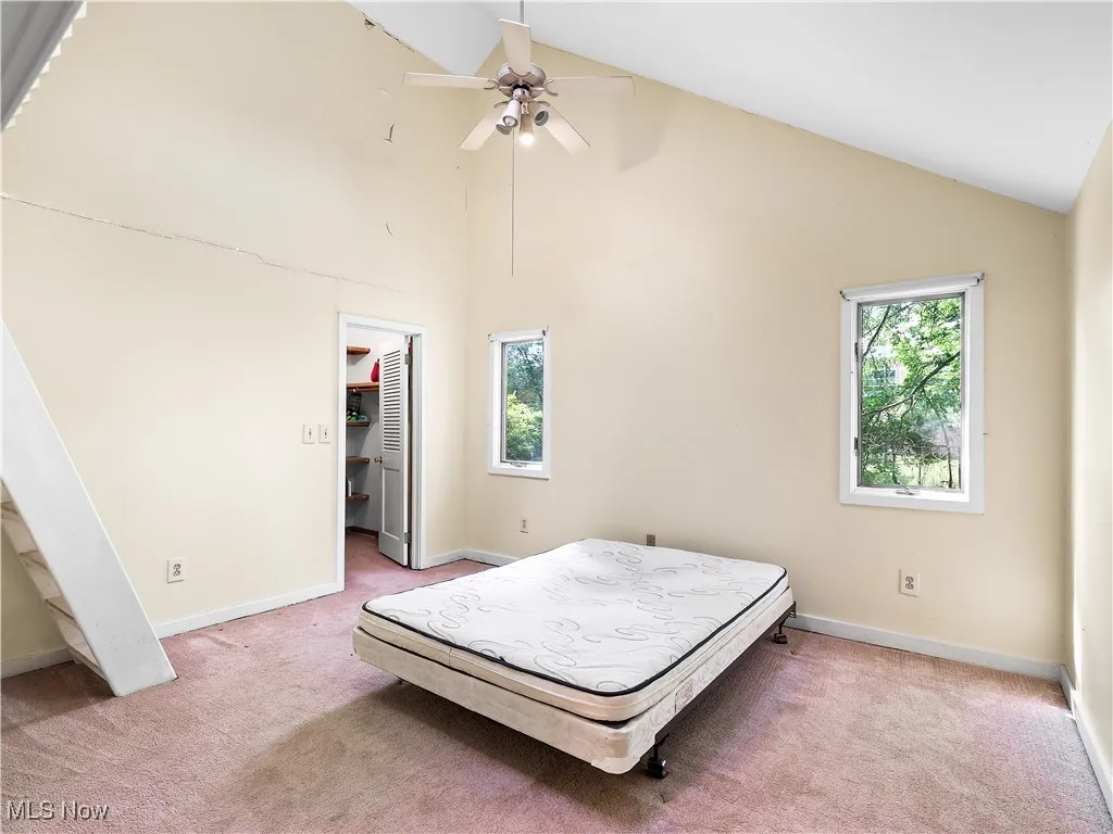 Bedroom with multiple windows, high vaulted ceiling, light carpet, a spacious closet, and ceiling fan