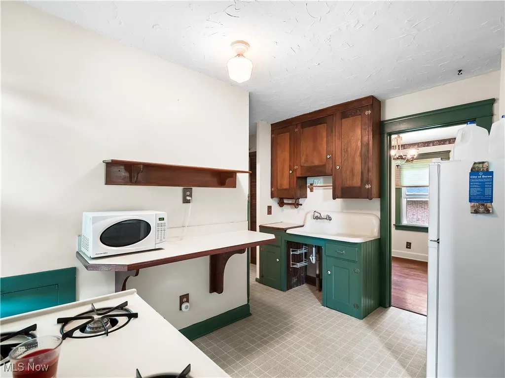 Kitchen with open shelves, light countertops, white appliances, green cabinets, and a chandelier