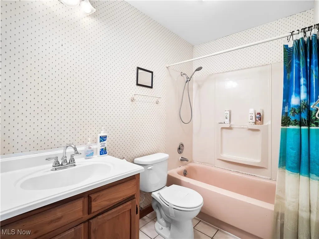 Full ensuite bathroom featuring shower / bath combo with shower curtain, light tile patterned flooring, and vanity