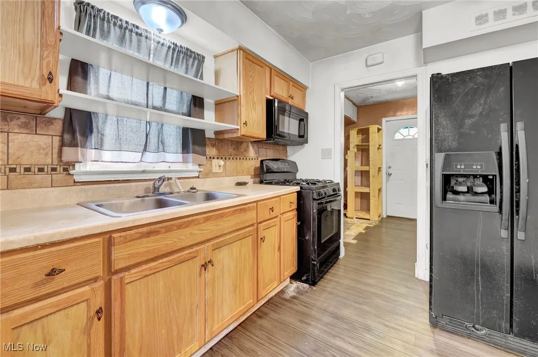 Kitchen featuring black appliances, decorative backsplash, light countertops, and light wood finished floors