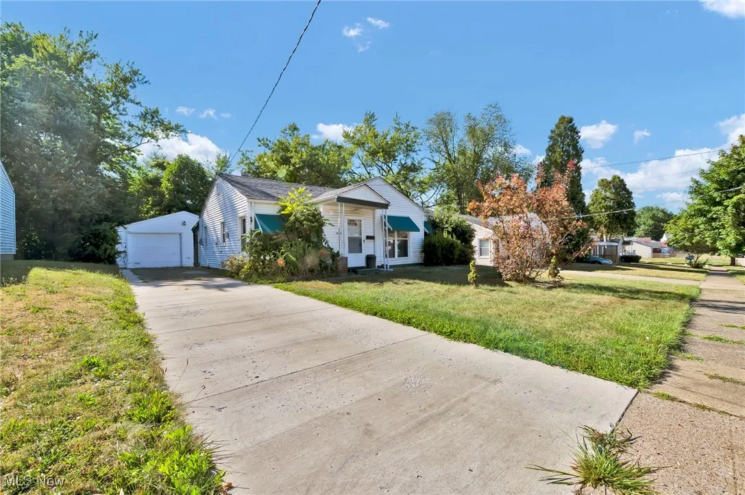 View of front of house with an outdoor structure, a front yard, a detached garage, and concrete driveway