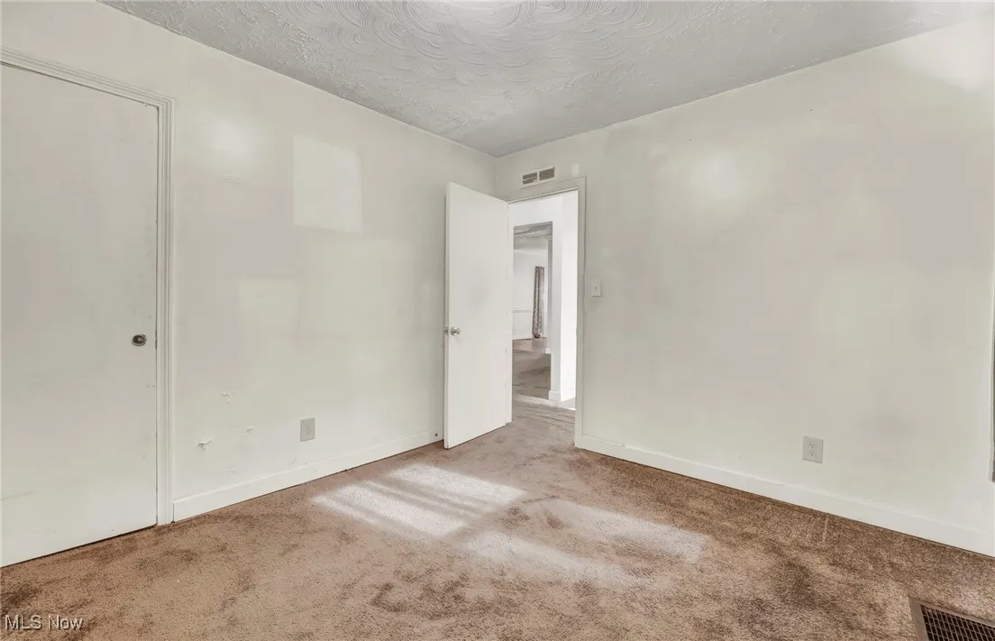 Carpeted empty room featuring a textured ceiling and baseboards
