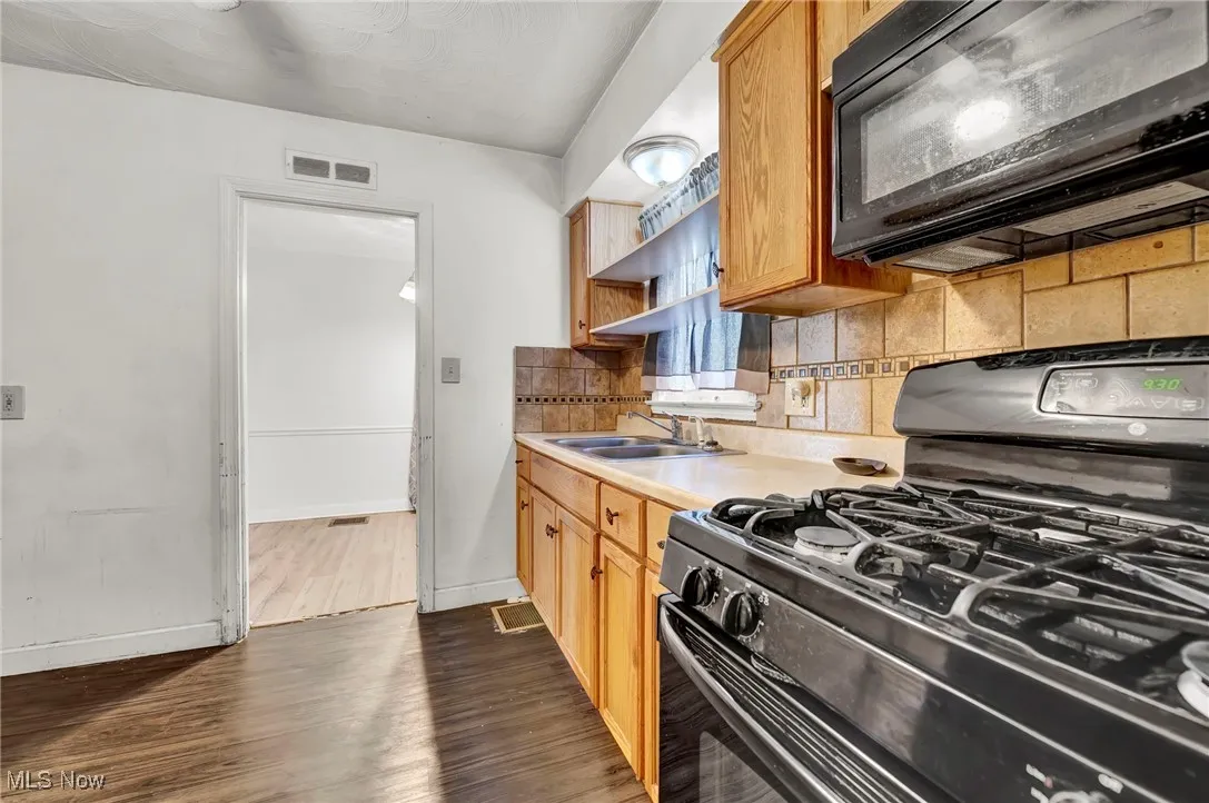Kitchen featuring black appliances, backsplash, light countertops, dark wood finished floors, and open shelves