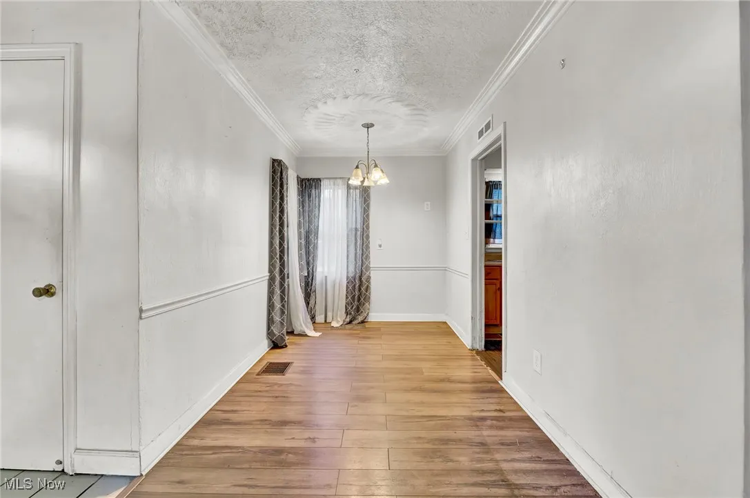 Unfurnished dining area with a textured ceiling, crown molding, wood-type flooring, and a chandelier