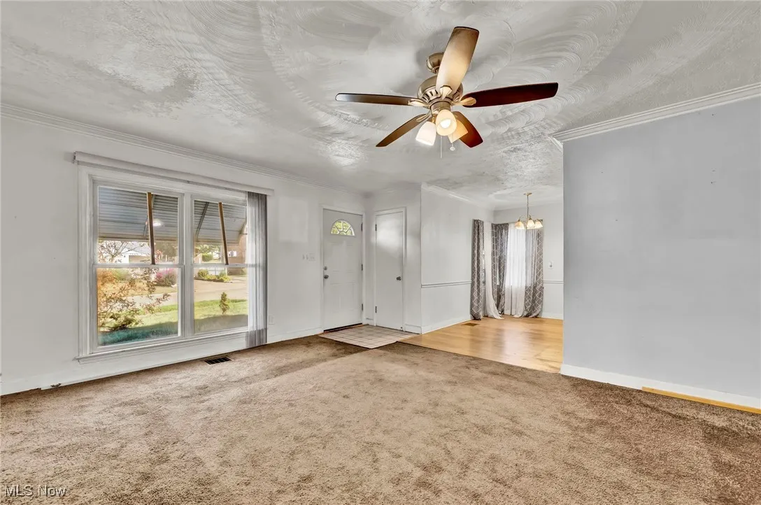 Unfurnished living room featuring light carpet, a ceiling fan, crown molding, a chandelier, and a textured ceiling