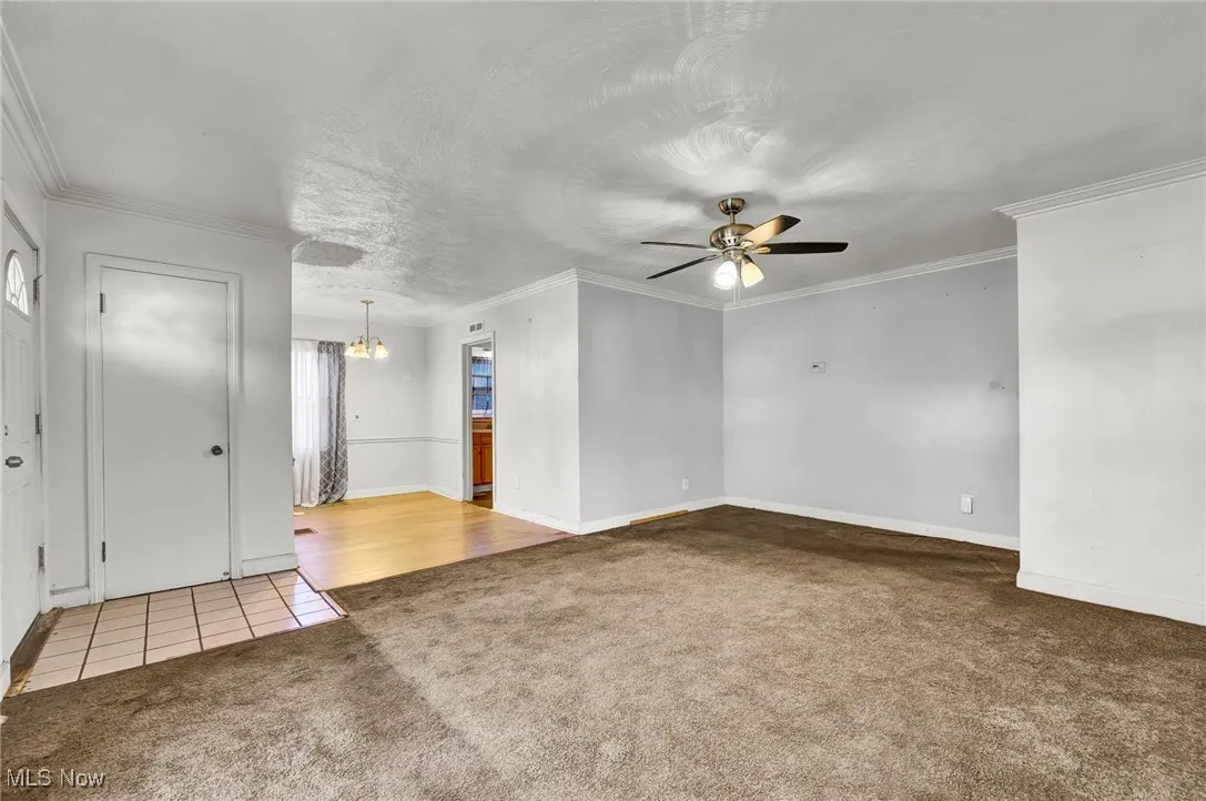 Empty room with light carpet, light tile patterned floors, ornamental molding, a ceiling fan, and a chandelier