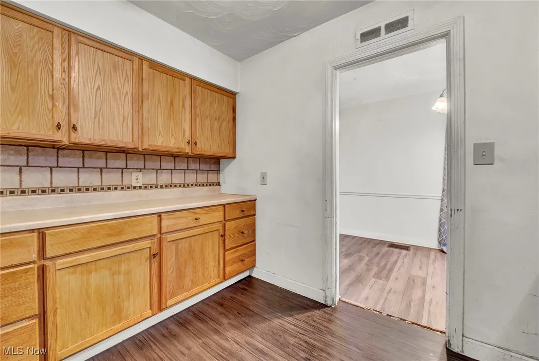 Kitchen with backsplash, light countertops, dark wood-style flooring, and light brown cabinets