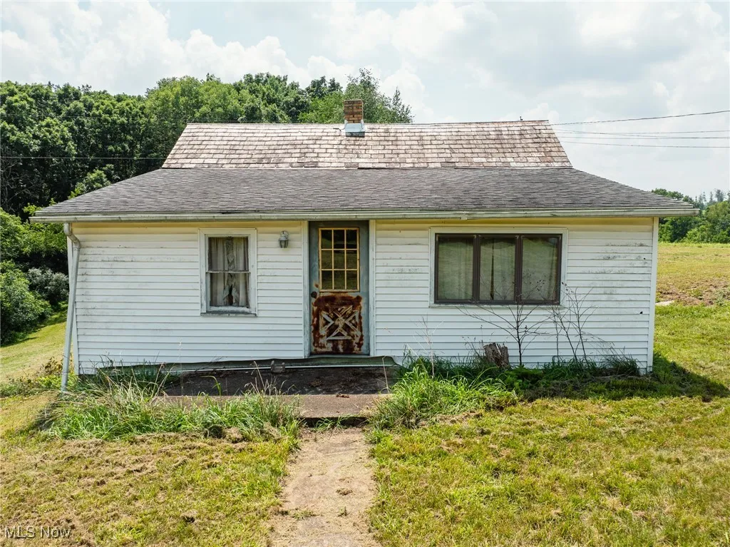 View of front facade with a front yard, a shingled roof, and a chimney