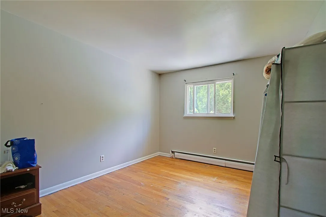 Unfurnished bedroom with light wood-style floors and baseboard heating