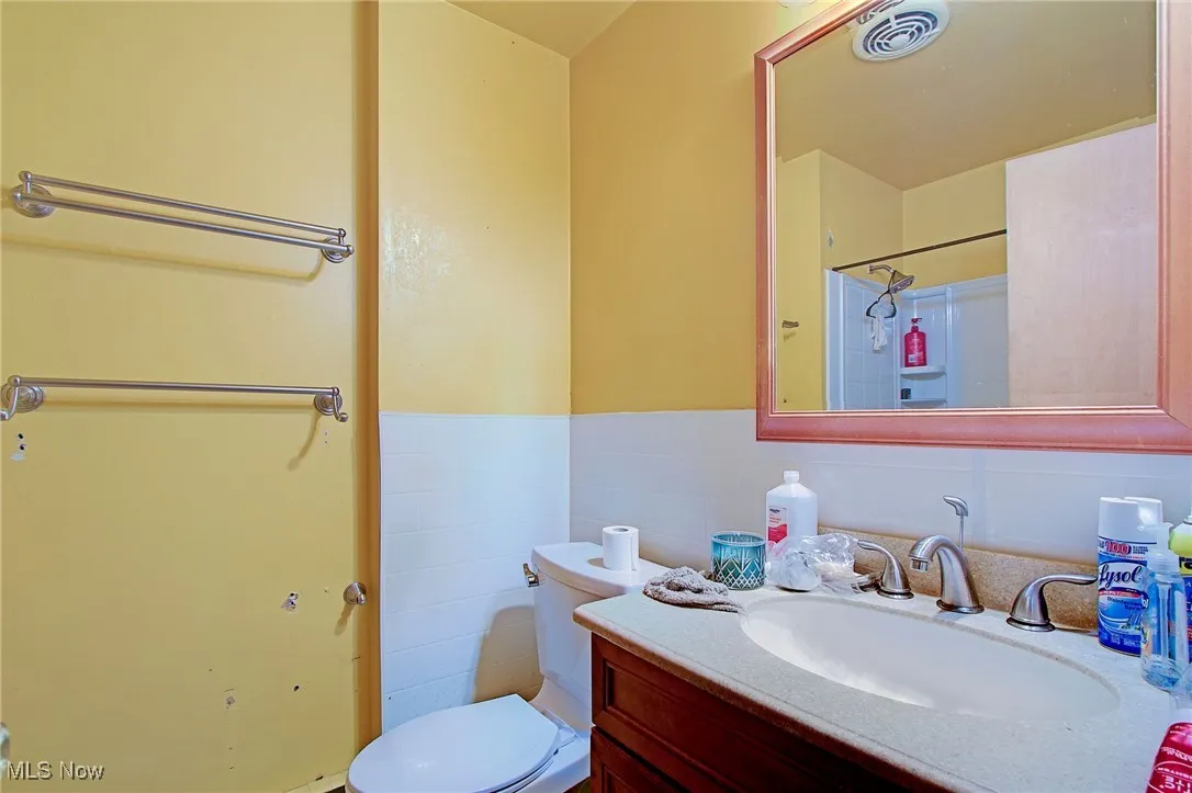 Bathroom featuring vanity, tile walls, a wainscoted wall, and a shower