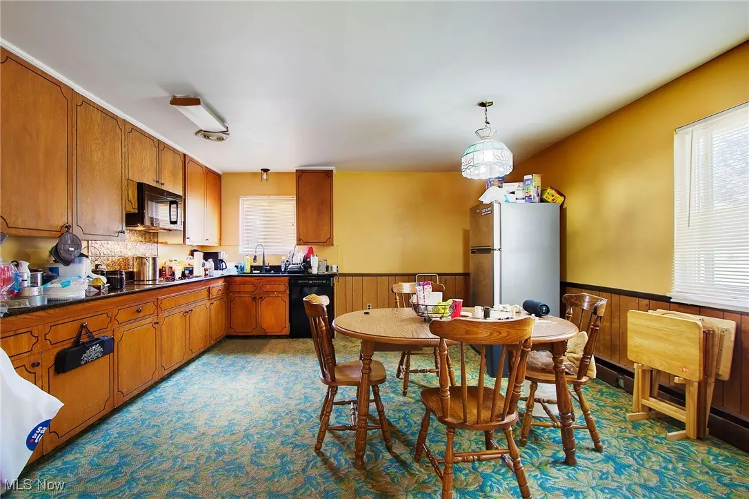 Kitchen featuring brown cabinetry, black appliances, dark countertops, wooden walls, and a wainscoted wall