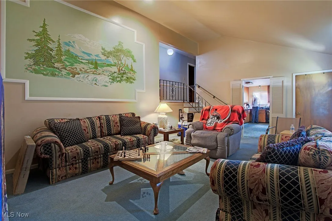 Living room featuring carpet, vaulted ceiling, and stairs