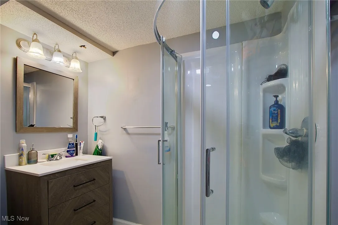 Bathroom featuring a textured ceiling, vanity, and a shower stall