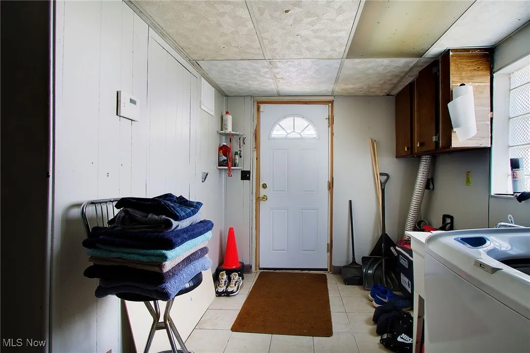 Washroom featuring washer / clothes dryer, light tile patterned floors, cabinet space, wood walls, and healthy amount of natural light