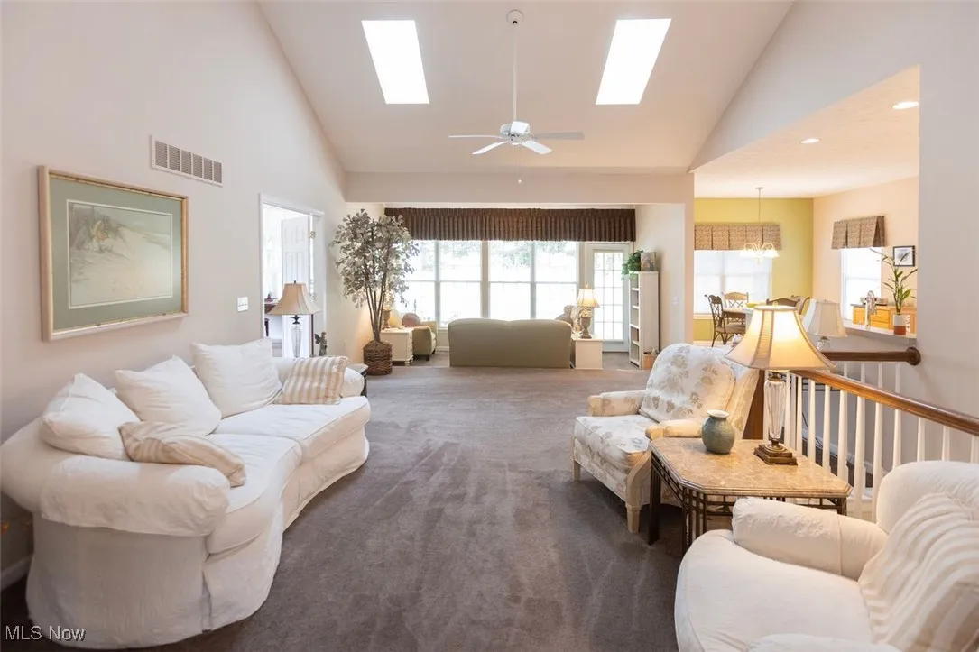 Great room with high vaulted ceiling, a ceiling fan, healthy amount of natural light, carpet, and a skylights