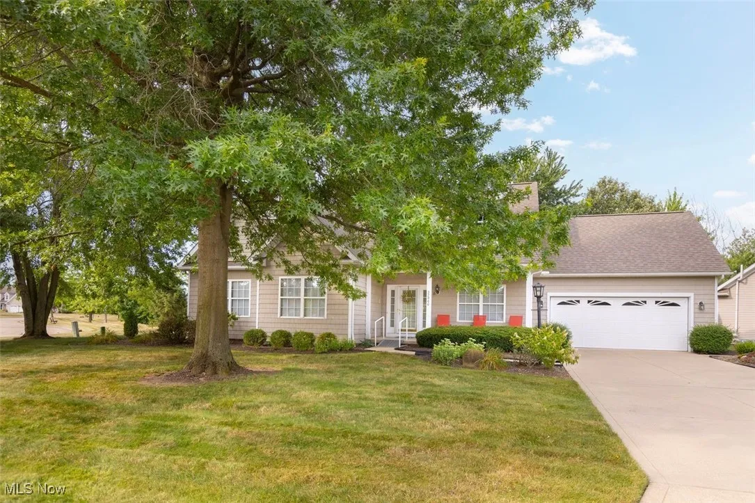 Cluster-ranch style home with an attached garage, driveway, a front yard, roof with shingles, and a porch