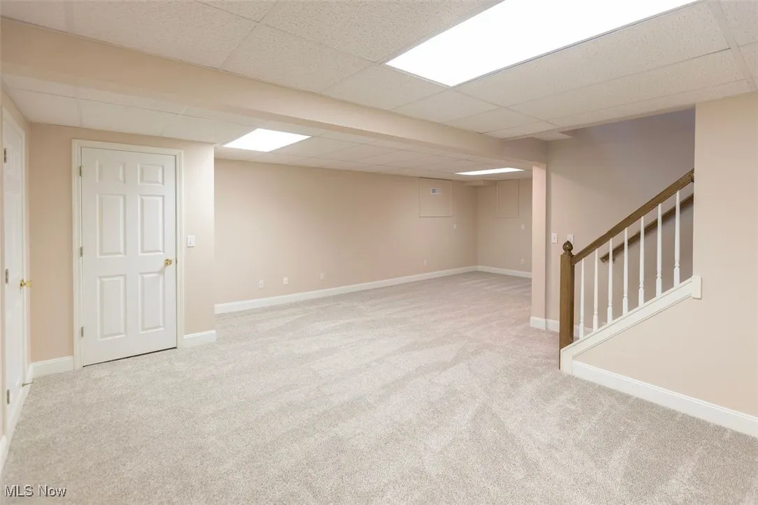 Finished rec room featuring light carpet, a paneled ceiling, and stairs