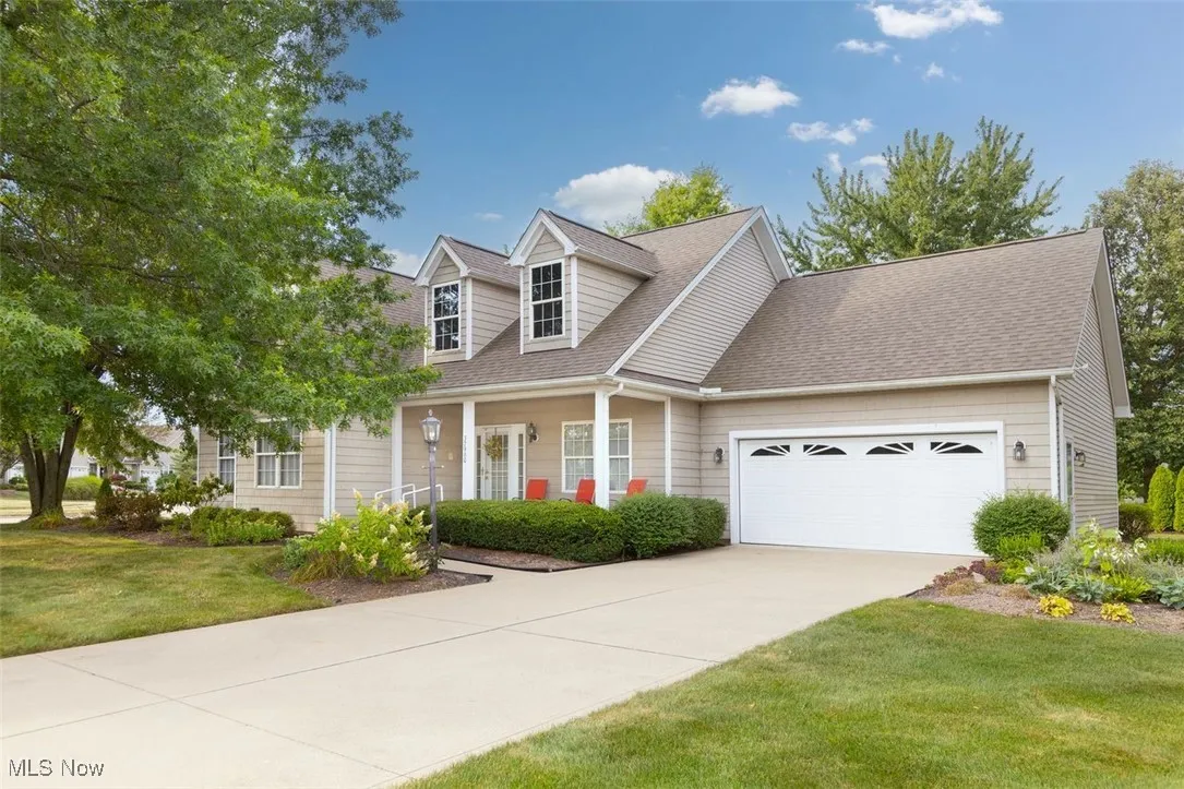 Cluster-ranch style home with an attached garage, a porch, roof with shingles, a front lawn, and driveway