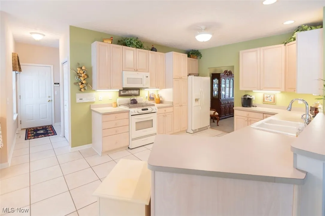 Kitchen with light tile patterned floors, white appliances, light countertops, a peninsula, and recessed lighting