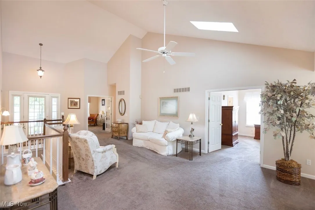 Great room featuring high vaulted ceiling, a skylight, carpet flooring, and a ceiling fan