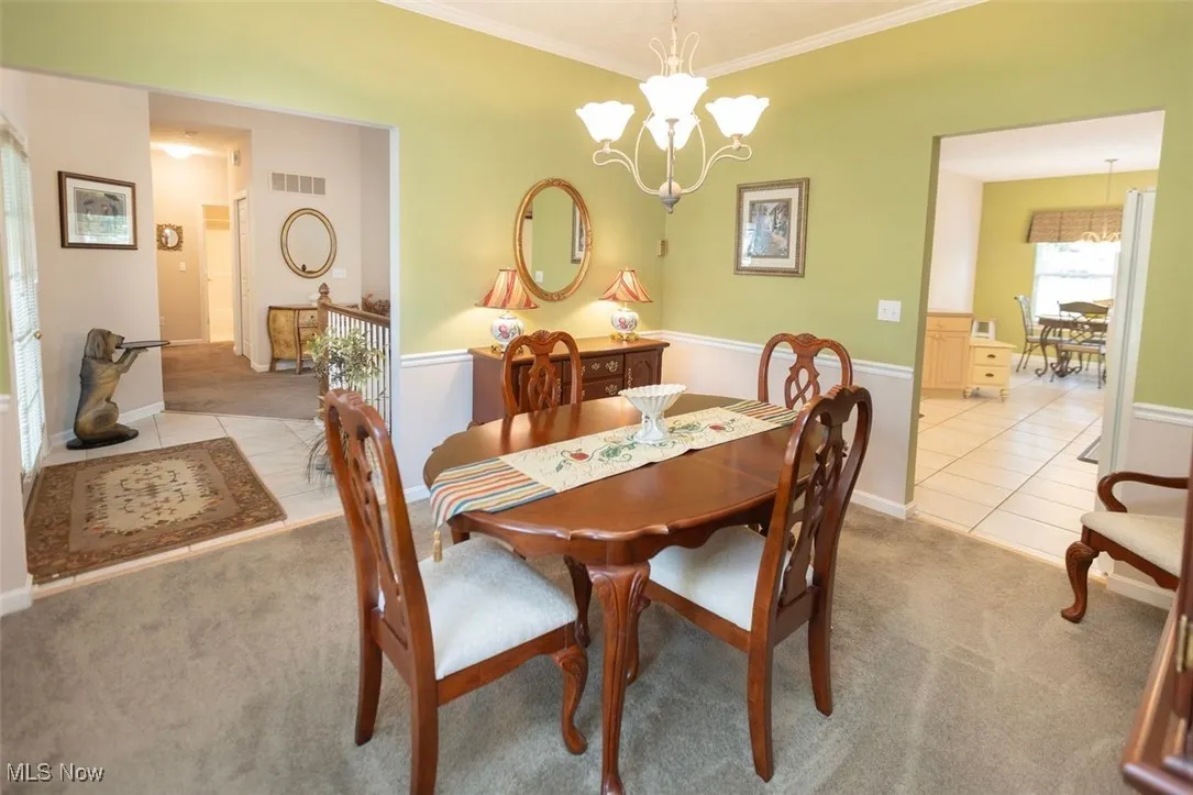 Dining room with light colored carpet, a chandelier, ornamental molding with a view to the front foyer and kitchen