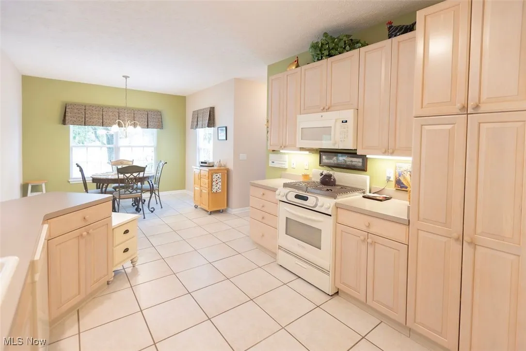 Kitchen featuring white appliances, light tile patterned flooring, decorative light fixtures, light countertops, and light cabinetry