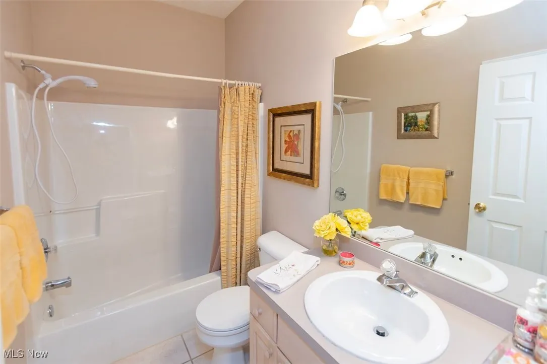 Full bath with shower / tub combo with curtain, vanity, and light tile patterned floors