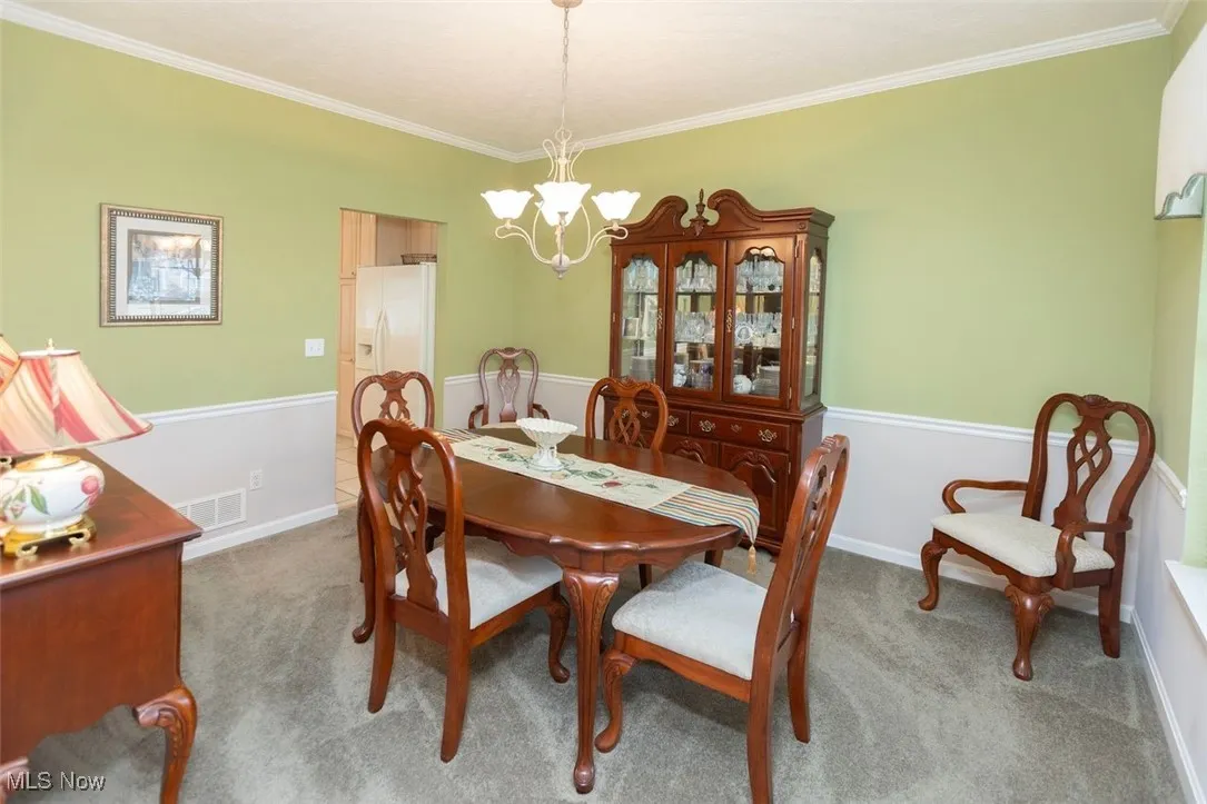 Carpeted dining room with crown molding and a chandelier