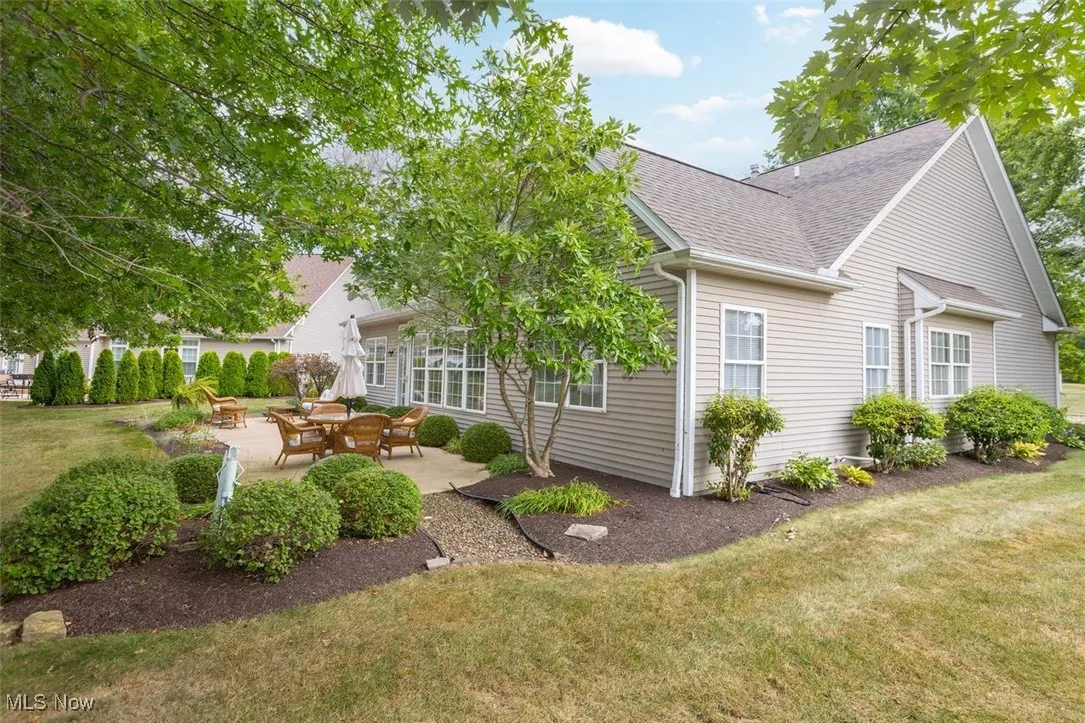 View of side of property featuring a patio, roof with shingles, and a yard