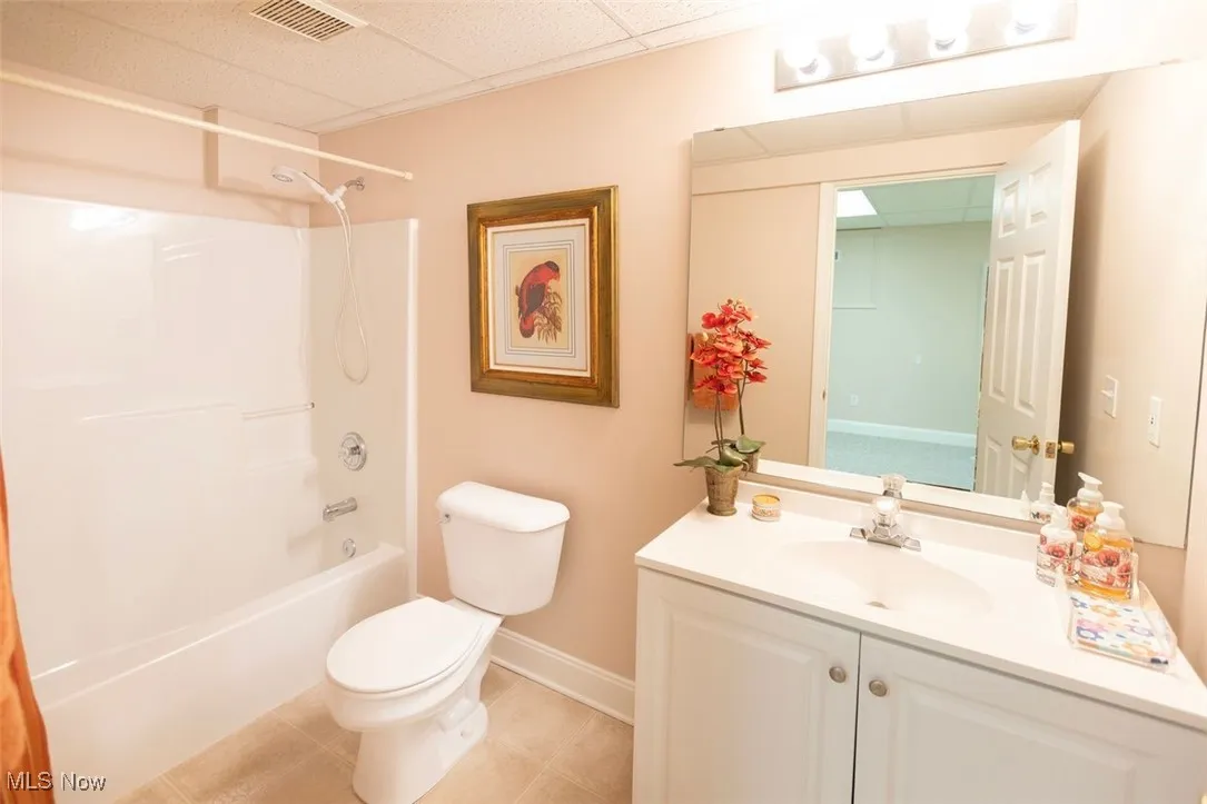 Basement full bathroom featuring a drop ceiling, bathing tub / shower combination, vanity, and light tile patterned flooring