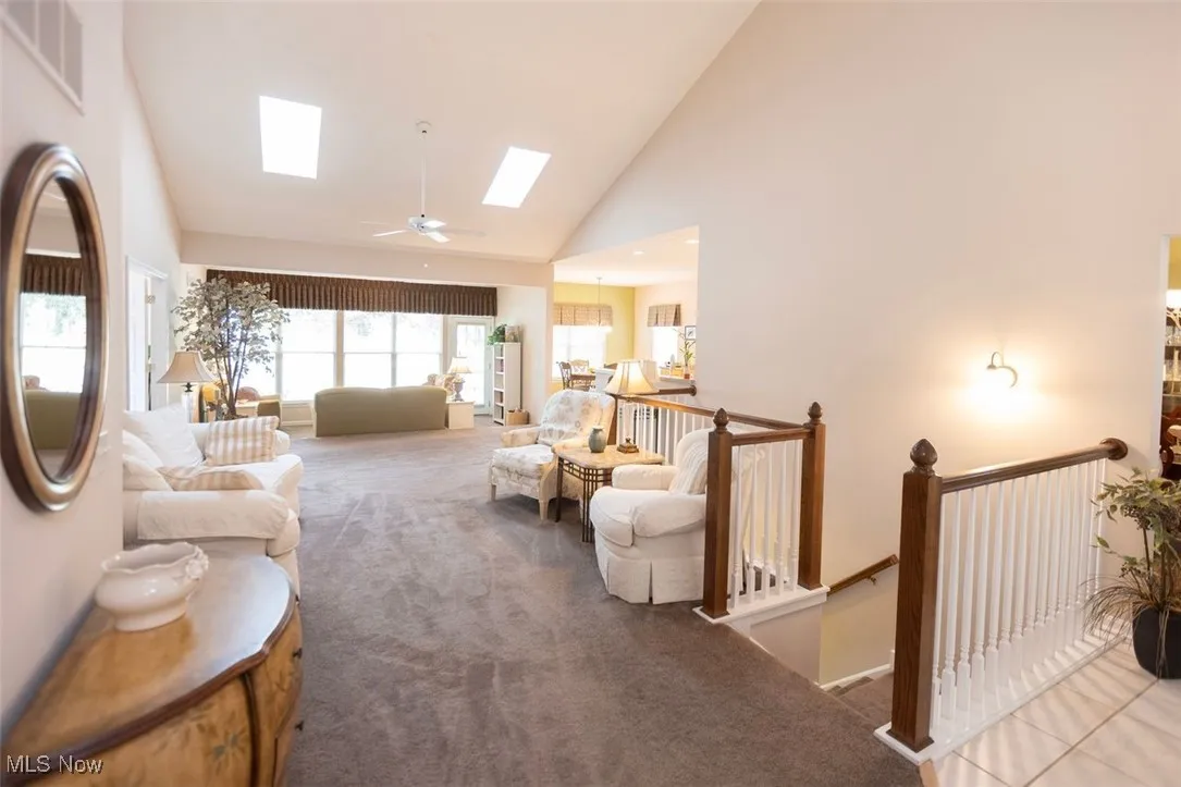 Carpeted great room featuring high vaulted ceiling, skylights, and ceiling fan