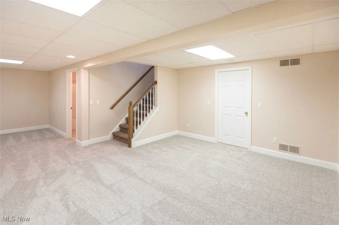 Finished rec room featuring light colored carpet, stairs, and a paneled ceiling