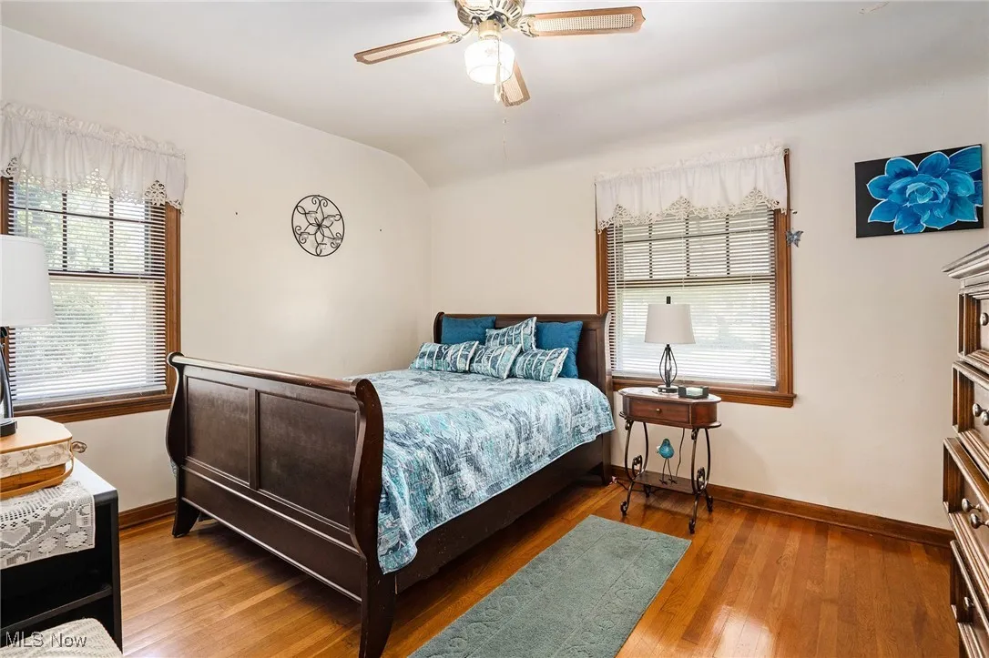 Bedroom featuring wood finished floors, multiple windows, a ceiling fan, and vaulted ceiling