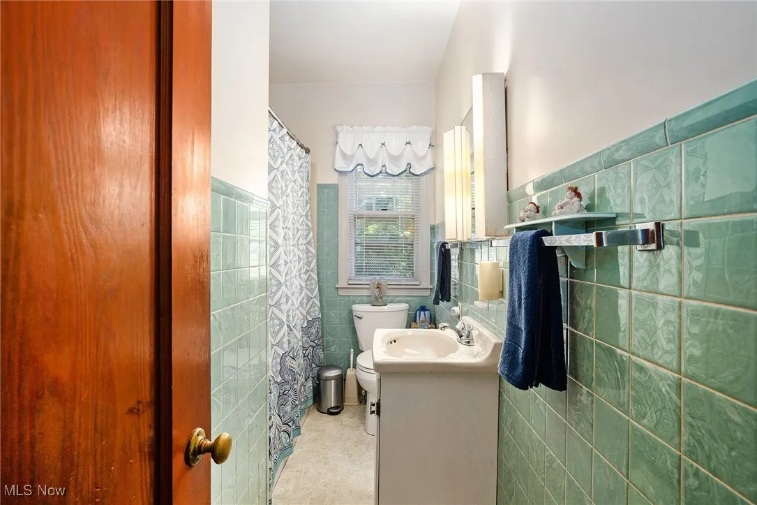 Bathroom featuring tile walls, vanity, wainscoting, curtained shower, and light tile patterned floors