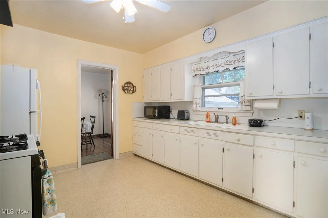 Kitchen with light countertops, white appliances, white cabinets, and a ceiling fan