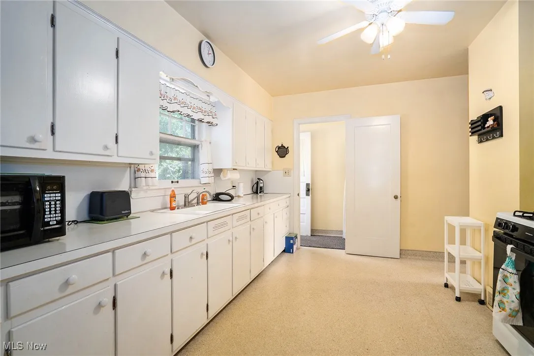 Kitchen featuring light countertops, black appliances, white cabinetry, light floors, and a ceiling fan