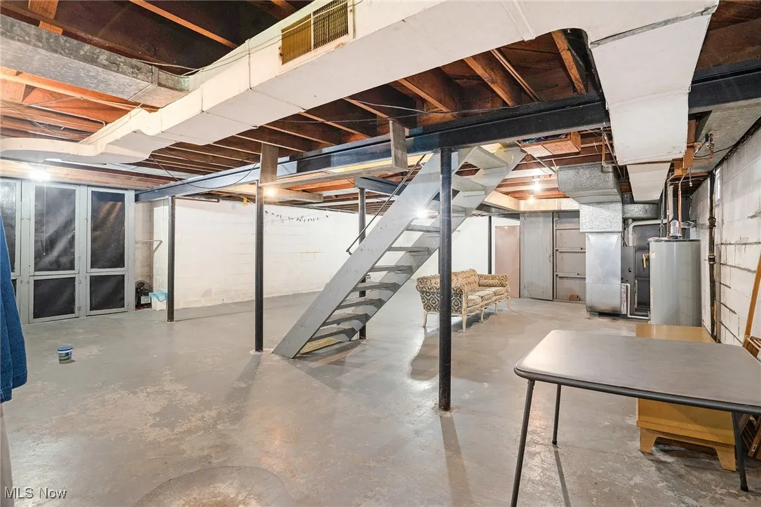 Unfinished basement with stairs, gas water heater, and heating unit