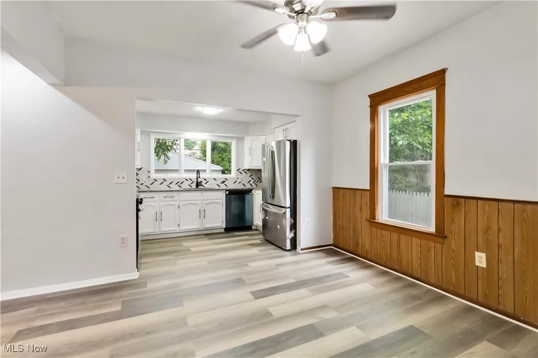Kitchen featuring appliances with stainless steel finishes, white cabinetry, plenty of natural light, light wood finished floors, and a wainscoted wall