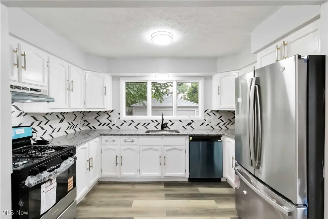 Kitchen featuring stainless steel appliances, light stone countertops, white cabinetry, and a textured ceiling