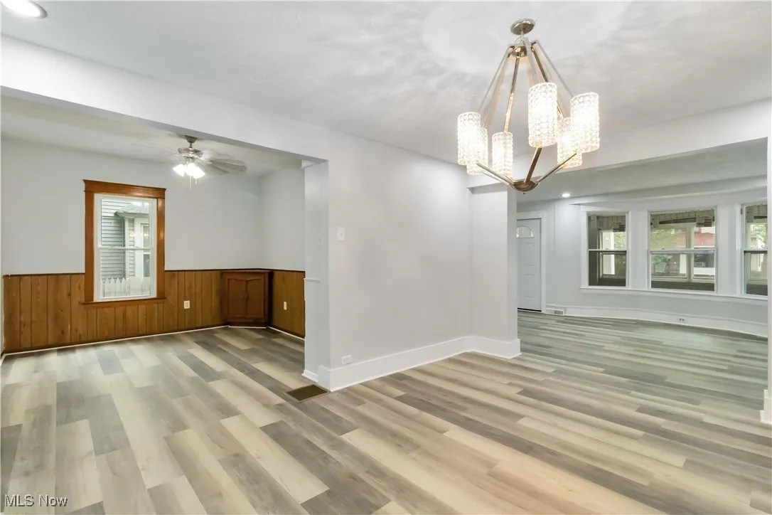 Empty room with light wood-style floors, a chandelier, a ceiling fan, wainscoting, and wood walls