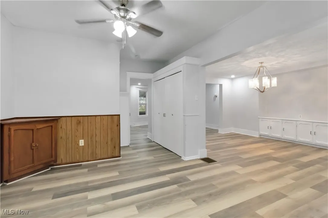 Empty room featuring a wainscoted wall, light wood-type flooring, ceiling fan, a chandelier, and wooden walls