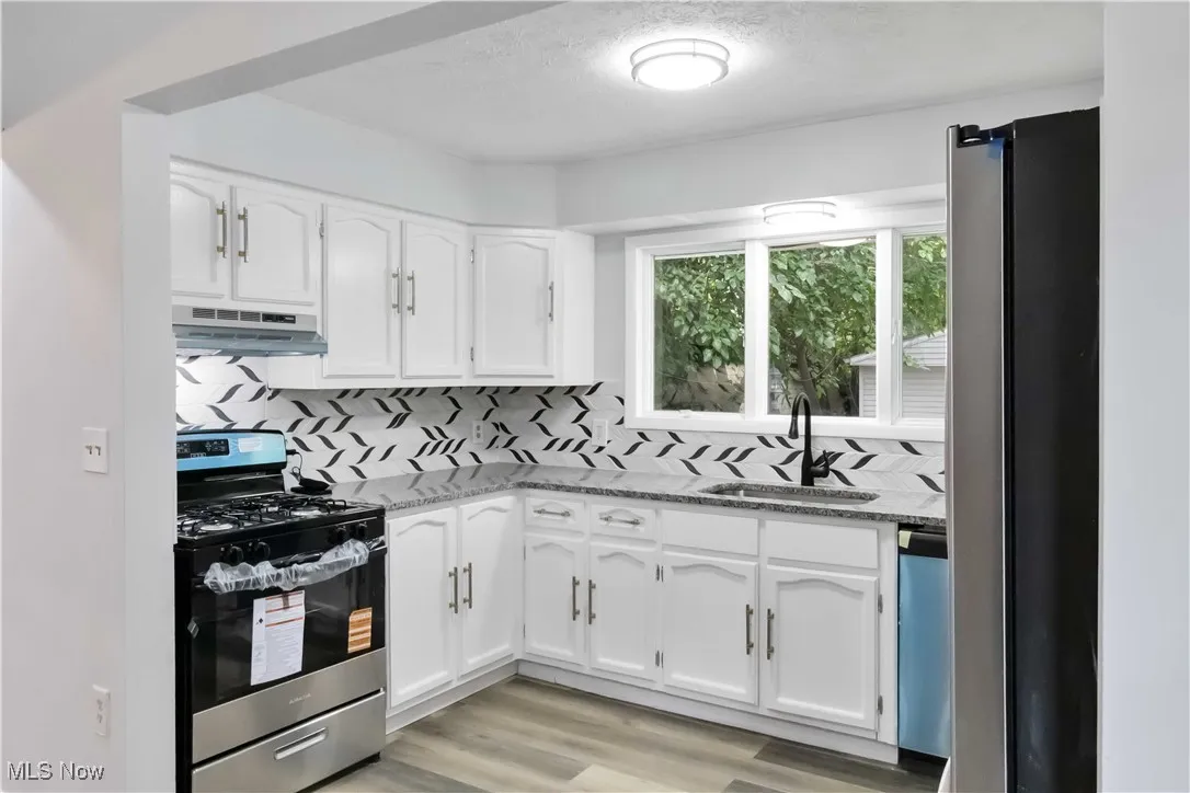 Kitchen featuring stainless steel appliances, tasteful backsplash, white cabinets, a textured ceiling, and light wood finished floors