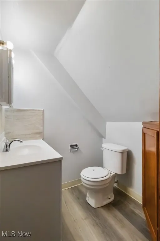 Half bath with vanity, vaulted ceiling, and wood finished floors